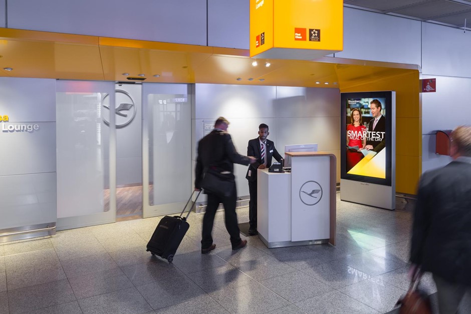 a man hands his boarding pass in, with a DOOH ad behind him